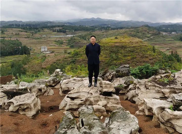 贵州省文物考古研究所副所长、三级研究员张合荣在普安大坡遗址，背后为铜鼓山遗址.jpg